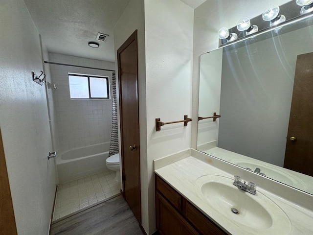 full bathroom with a textured ceiling, shower / bathtub combination with curtain, hardwood / wood-style floors, toilet, and vanity