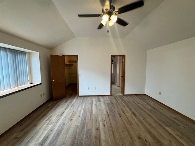 unfurnished bedroom with a closet, wood-type flooring, ceiling fan, a spacious closet, and lofted ceiling