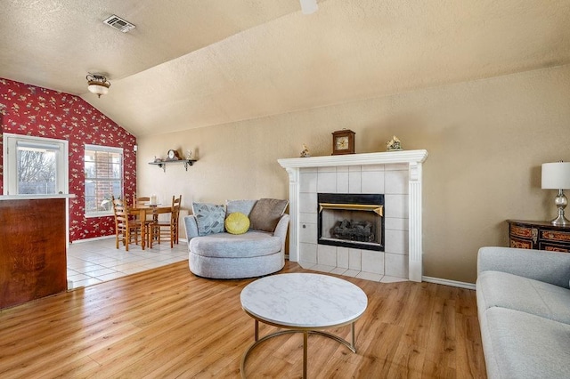 living room with vaulted ceiling, a tiled fireplace, a textured ceiling, and light hardwood / wood-style floors