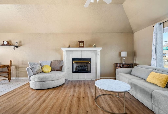 living room featuring ceiling fan, light wood-type flooring, vaulted ceiling, and a fireplace