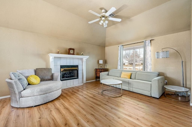 living room with a tiled fireplace, ceiling fan, vaulted ceiling, and light hardwood / wood-style floors