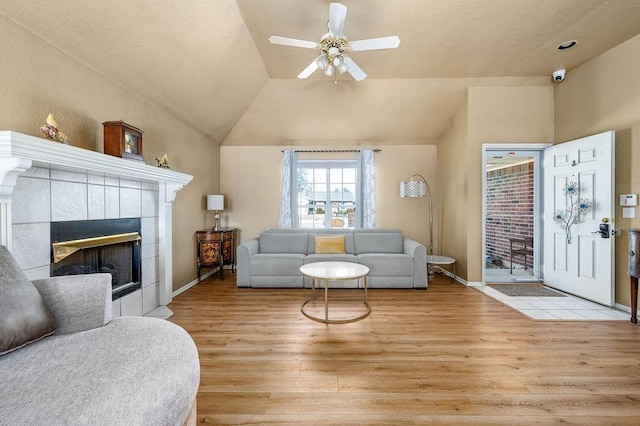 living room with lofted ceiling, a tile fireplace, light wood-type flooring, and ceiling fan