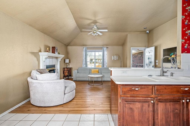 living room featuring vaulted ceiling, light tile patterned floors, a fireplace, ceiling fan, and sink