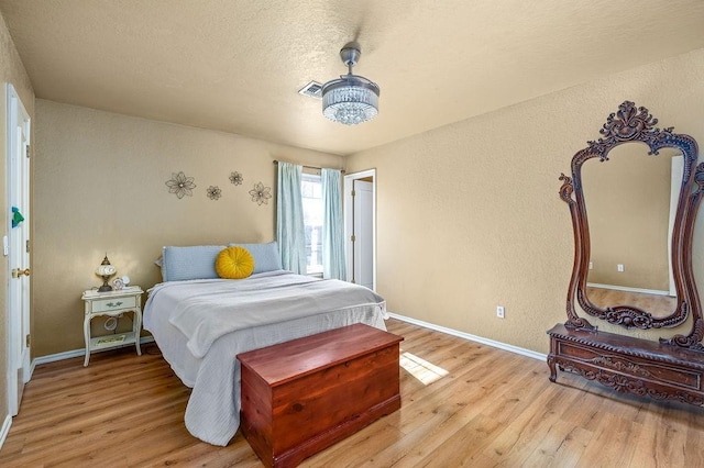 bedroom with a notable chandelier, light wood-type flooring, and a textured ceiling