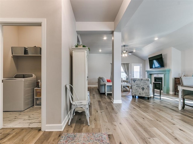 interior space with washer / clothes dryer, light hardwood / wood-style floors, vaulted ceiling, ceiling fan, and a tiled fireplace