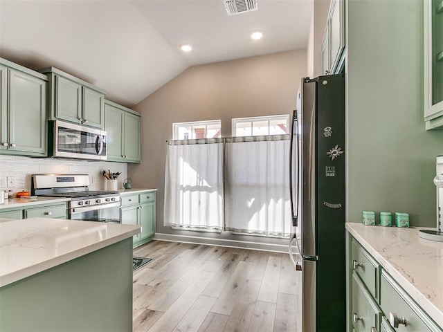 kitchen with light stone counters, lofted ceiling, stainless steel appliances, and green cabinetry