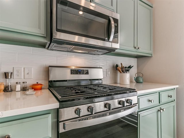 kitchen with backsplash, green cabinets, and stainless steel appliances