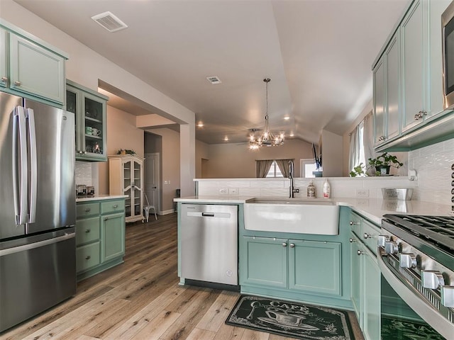 kitchen with backsplash, vaulted ceiling, kitchen peninsula, sink, and stainless steel appliances