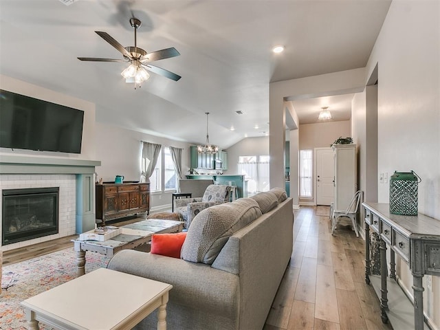 living room featuring light wood-type flooring, a healthy amount of sunlight, vaulted ceiling, and a brick fireplace