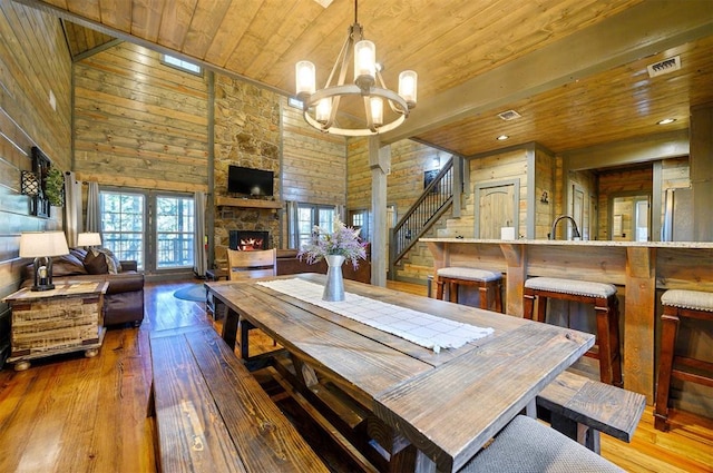 dining area with wood ceiling, light hardwood / wood-style flooring, an inviting chandelier, a towering ceiling, and a fireplace