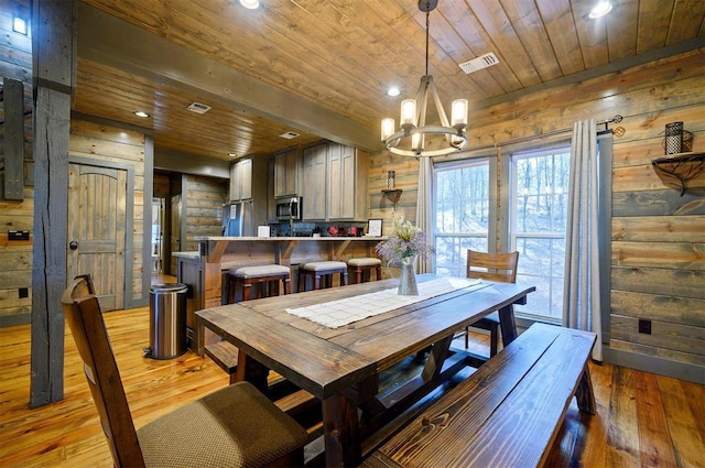 dining space featuring wood walls, a chandelier, light hardwood / wood-style floors, and wooden ceiling