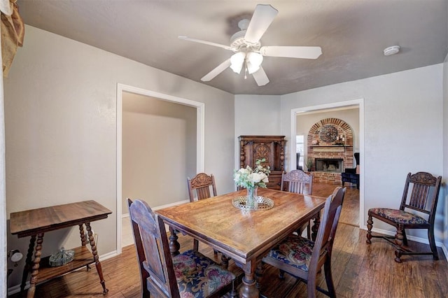 dining room with ceiling fan, a brick fireplace, and hardwood / wood-style floors