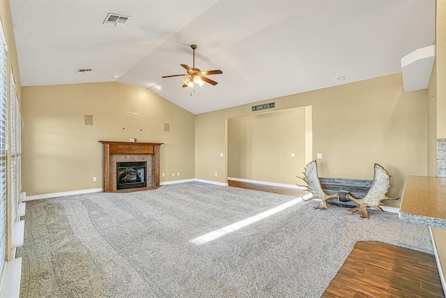 living room with vaulted ceiling, ceiling fan, a tiled fireplace, and hardwood / wood-style flooring