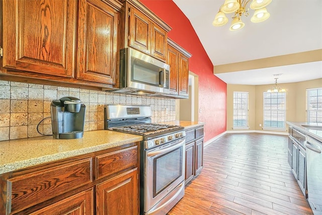 kitchen featuring decorative light fixtures, a notable chandelier, decorative backsplash, light wood-type flooring, and stainless steel appliances