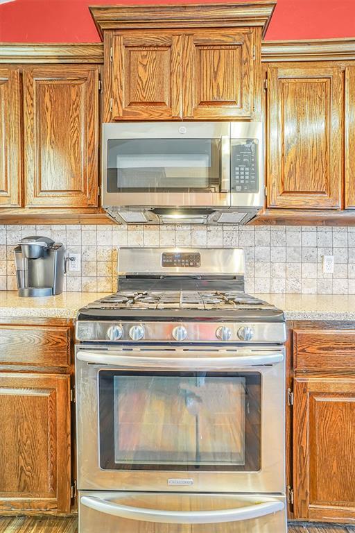 kitchen with dark wood-type flooring, appliances with stainless steel finishes, and tasteful backsplash