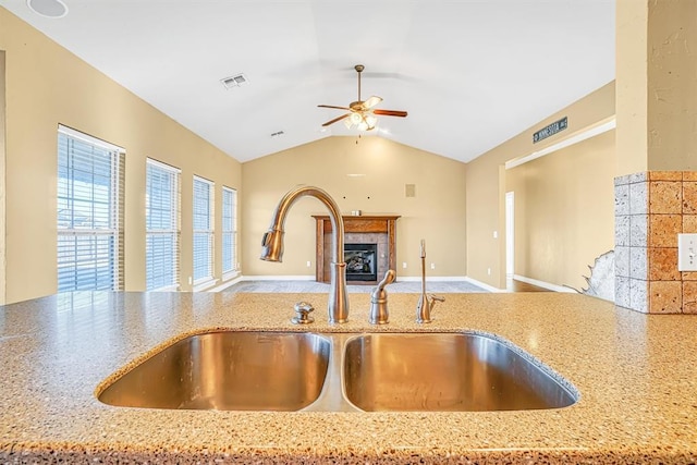 kitchen with ceiling fan, a fireplace, light stone countertops, vaulted ceiling, and sink