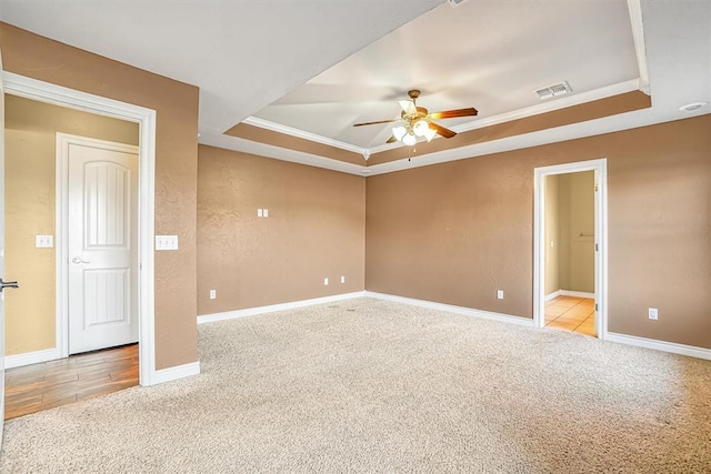 empty room featuring ceiling fan, ornamental molding, light colored carpet, and a raised ceiling