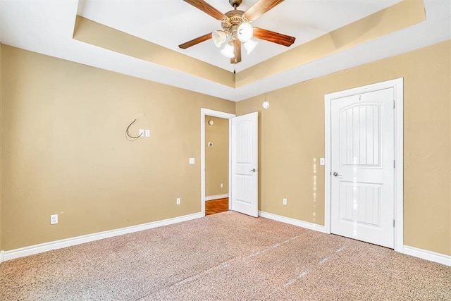 unfurnished bedroom with ceiling fan, a tray ceiling, and carpet floors