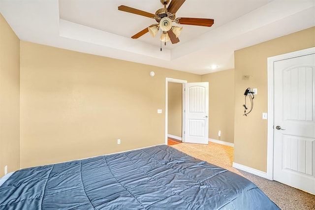 unfurnished bedroom with ceiling fan, a tray ceiling, and carpet flooring