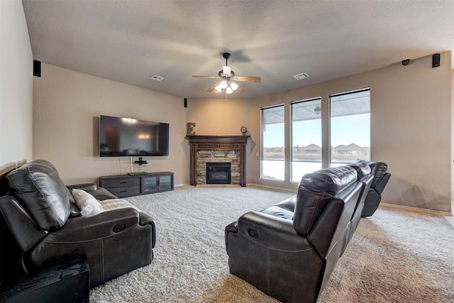 living room featuring ceiling fan, a stone fireplace, light carpet, and a textured ceiling