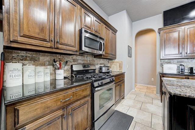 kitchen with dark stone counters, stainless steel appliances, backsplash, and light tile patterned floors