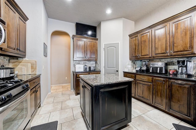 kitchen featuring a center island, dark stone countertops, light tile patterned floors, stainless steel gas range oven, and backsplash