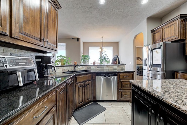 kitchen featuring sink, a textured ceiling, light tile patterned floors, dark stone counters, and appliances with stainless steel finishes