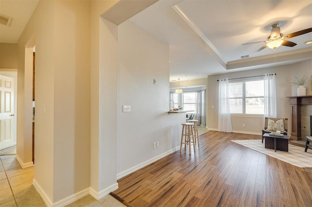 living room with a tiled fireplace, light hardwood / wood-style floors, crown molding, ceiling fan, and a tray ceiling