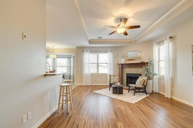 sitting room featuring a tiled fireplace, ceiling fan, hardwood / wood-style flooring, a tray ceiling, and crown molding