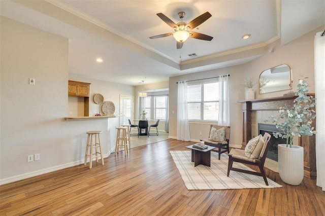 living area featuring crown molding, a tile fireplace, ceiling fan, and light hardwood / wood-style flooring