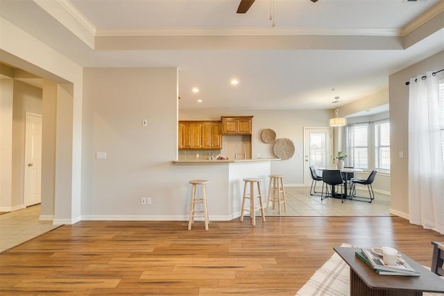 kitchen with a kitchen breakfast bar, a raised ceiling, light wood-type flooring, kitchen peninsula, and ceiling fan