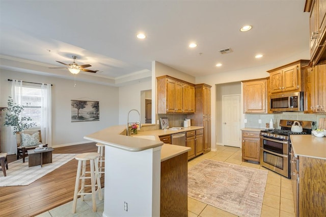 kitchen with ceiling fan, light tile patterned floors, kitchen peninsula, a breakfast bar, and appliances with stainless steel finishes