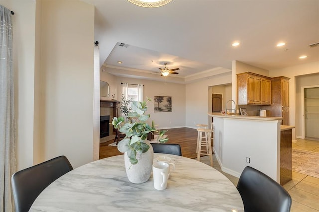 dining space featuring ceiling fan, light tile patterned flooring, a raised ceiling, and sink