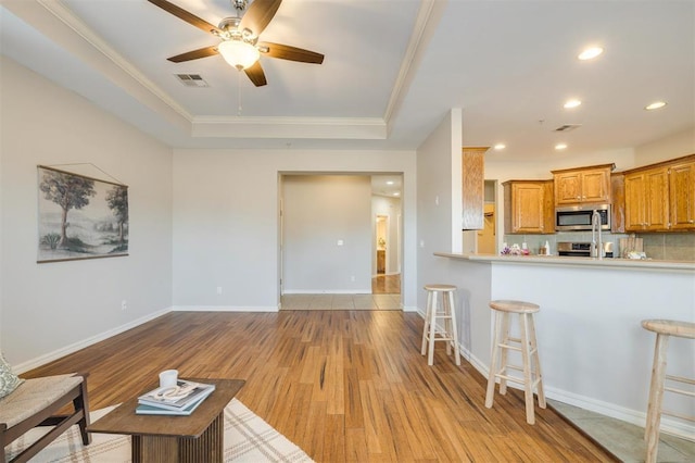 living room with ornamental molding, a raised ceiling, ceiling fan, and light hardwood / wood-style floors