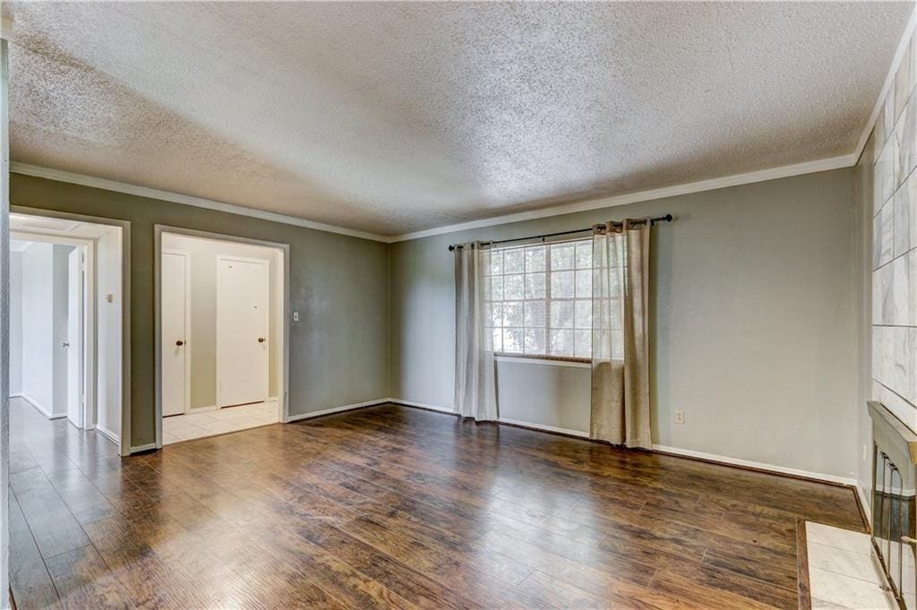 unfurnished living room with a textured ceiling, ornamental molding, and dark hardwood / wood-style floors