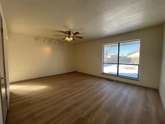 empty room featuring dark hardwood / wood-style flooring, a textured ceiling, ceiling fan, and rail lighting