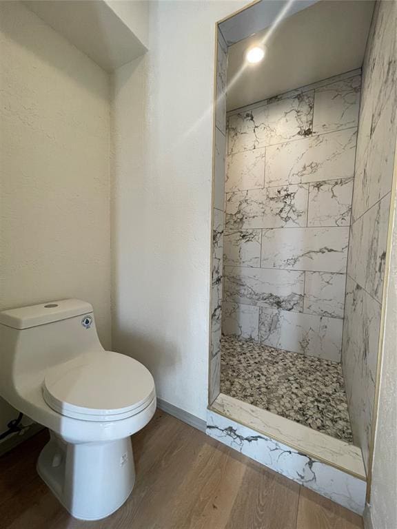 bathroom featuring toilet, tiled shower, and hardwood / wood-style floors