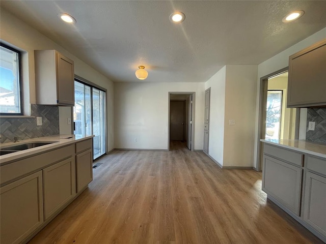 kitchen with light hardwood / wood-style floors, gray cabinetry, a textured ceiling, sink, and backsplash