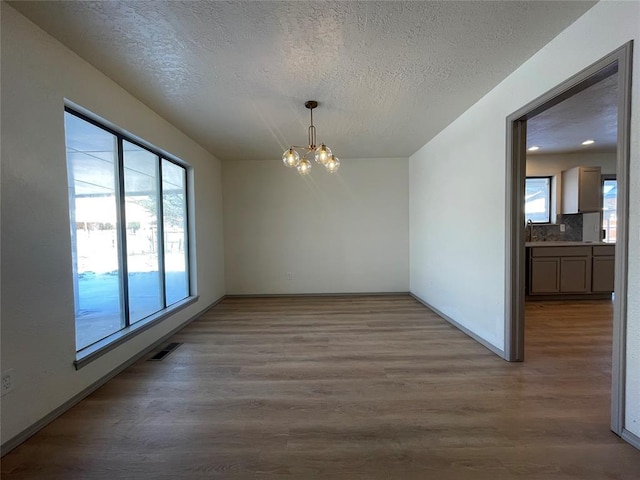 unfurnished dining area with plenty of natural light, a textured ceiling, a chandelier, and hardwood / wood-style floors