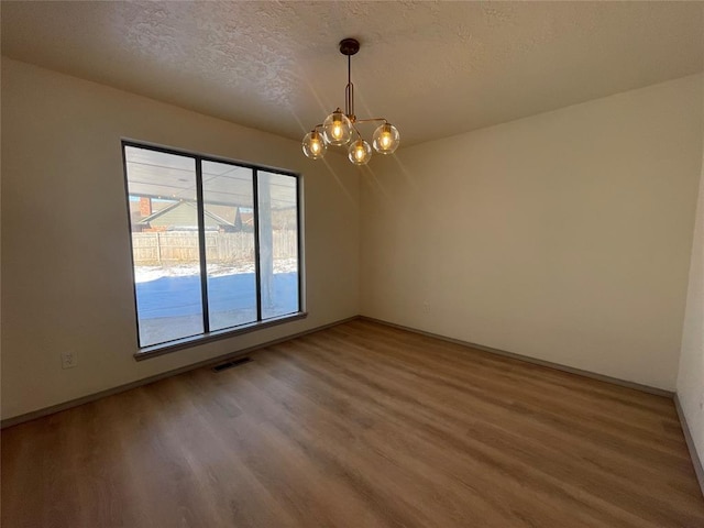 empty room with a textured ceiling, hardwood / wood-style floors, and a notable chandelier