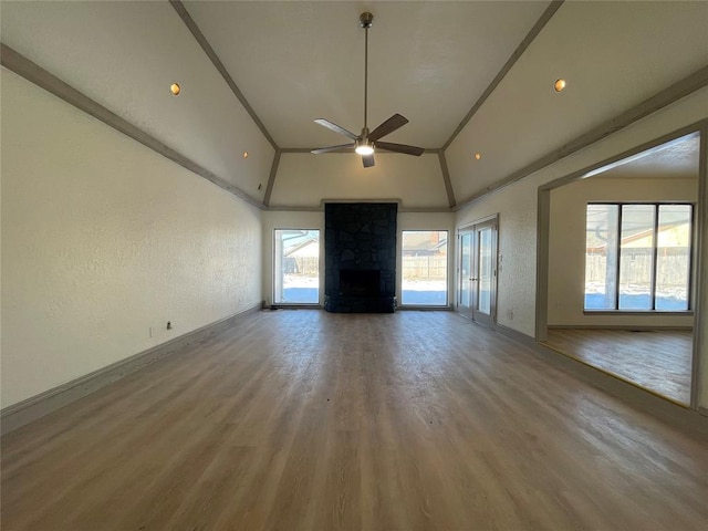 unfurnished living room with vaulted ceiling, ceiling fan, wood-type flooring, crown molding, and a stone fireplace