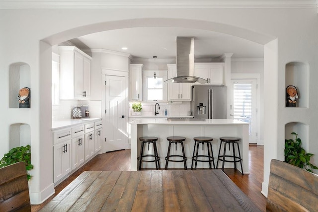 kitchen with island exhaust hood, hanging light fixtures, stainless steel fridge, a kitchen island, and white cabinets