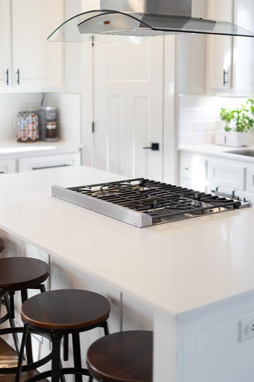 kitchen with a breakfast bar, white cabinetry, wall chimney range hood, and stainless steel gas cooktop