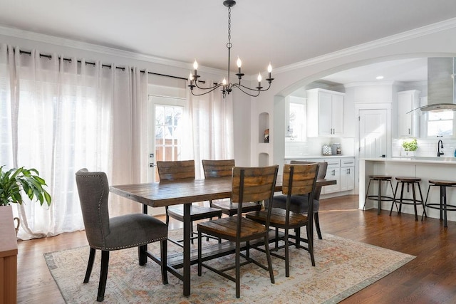 dining space featuring sink, an inviting chandelier, crown molding, and dark wood-type flooring