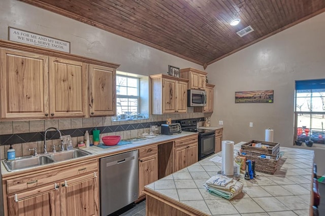 kitchen with vaulted ceiling, appliances with stainless steel finishes, sink, backsplash, and tile counters