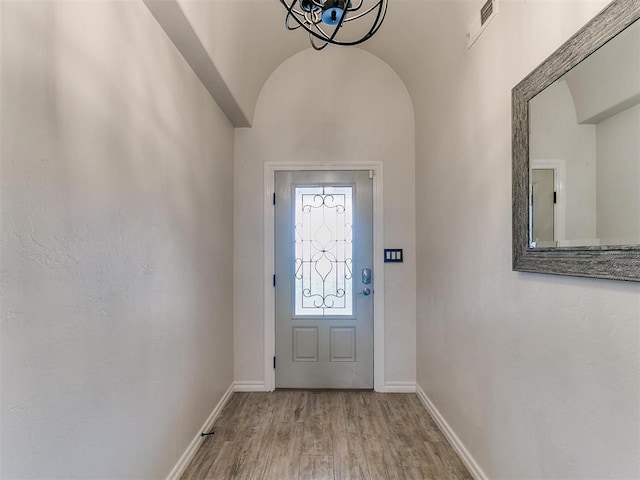 entrance foyer featuring vaulted ceiling, an inviting chandelier, brick ceiling, and wood-type flooring