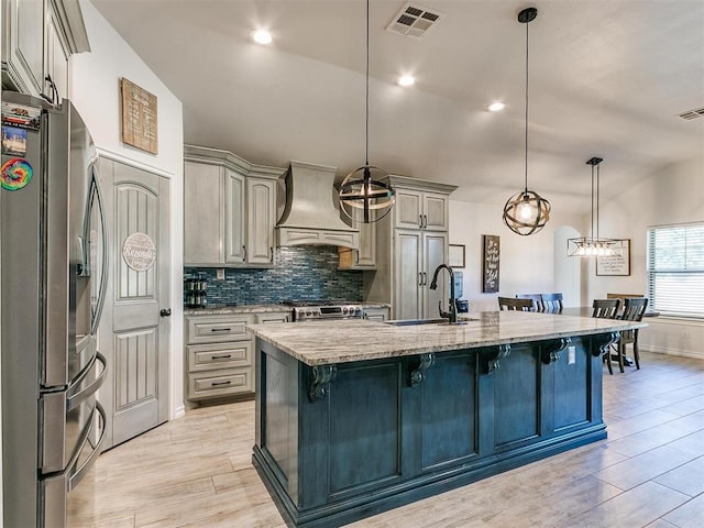 kitchen with custom exhaust hood, an island with sink, appliances with stainless steel finishes, hanging light fixtures, and sink