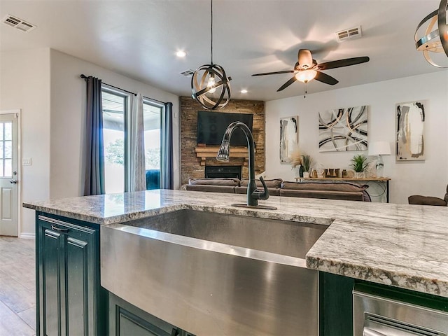 kitchen featuring decorative light fixtures, a fireplace, sink, and light stone counters