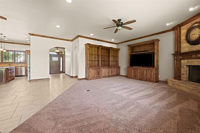 unfurnished living room featuring ceiling fan, crown molding, and a stone fireplace