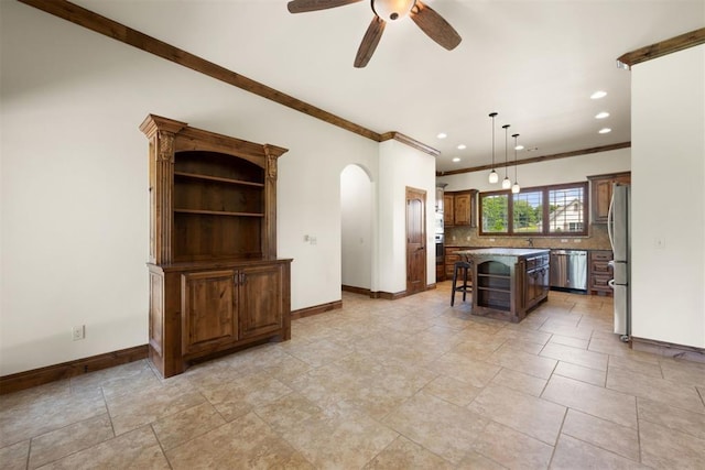 kitchen with a kitchen bar, ceiling fan, a kitchen island, crown molding, and appliances with stainless steel finishes